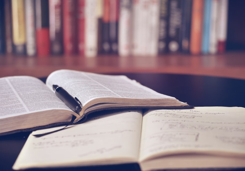 Student taking notes while studying at a desk surrounded by books